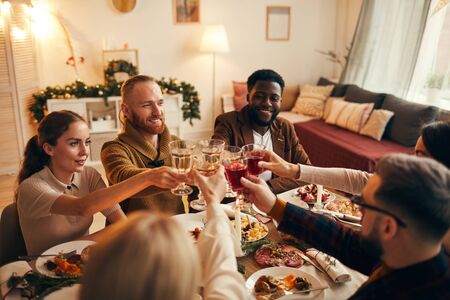 Multi-ethnic group of young people clinking champagne glasses while enjoying Christmas dinner at home, copy spaceの写真素材