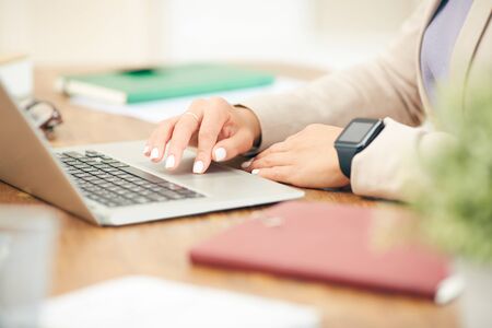 Side view closeup of unrecognizable businesswoman using laptop while working at desk in office, focus on female hands typing on keyboardの写真素材