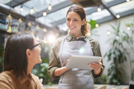 Waist up portrait of young waitress holding digital tablet while taking order of client at outdoor cafe terrace, copy spaceの写真素材
