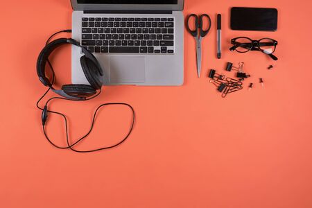 Above view of laptop computer and headphones at office workplace with coral background, copy space