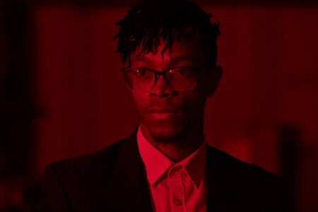 Head and shoulders portrait of trendy African-American man wearing glasses posing looking away in...
