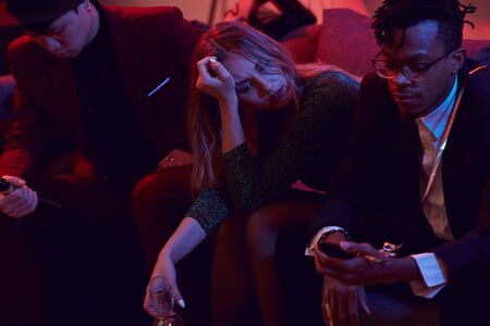 Portrait of sad young woman holding champagne glass while siting on sofa during nightclub party