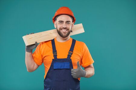 Horizontal waist up studio shot of young man holding wooden plank and showing thumb up looking at cameraの写真素材