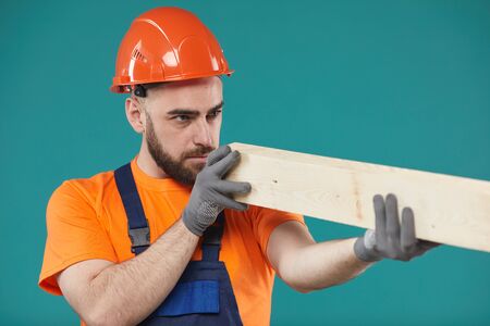 Horizontal studio medium portrait shot of manual worker wearing uniform checking quality of wooden plankの写真素材
