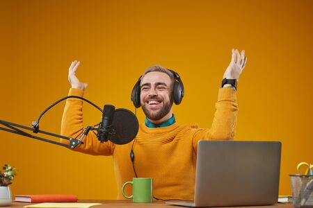 Horizontal studio portrait of emotional radio presenter wearing stylish casual clothes sitting at desk recording broadcastの写真素材