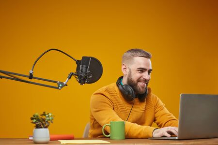 Horizontal medium studio shot of happy young Caucasian man typing something on his laptop, mustard backgroundの写真素材
