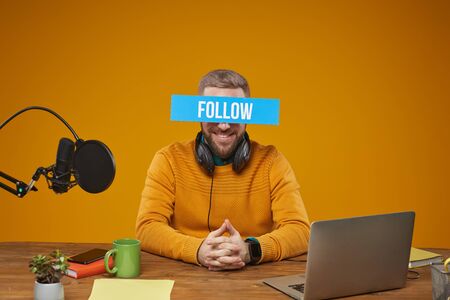Horizontal studio shot of modern video blogger wearing stylish casual clothes sitting at desk with...