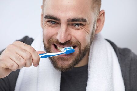 Horizontal close up portrait shot of yong man with beard on face brushing his teeth in the morningの写真素材