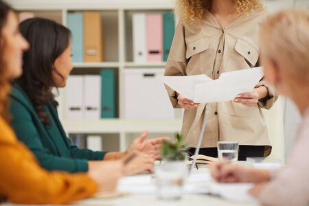 Unrecognizable woman standing in front of her colleagues holding papers discussing business strategy with themの写真素材