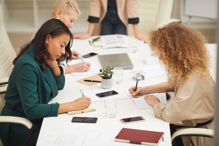 Group of creative businesswomen brainstorming at meeting writing down their ideas in notebooks, horizontal high angle shotの写真素材
