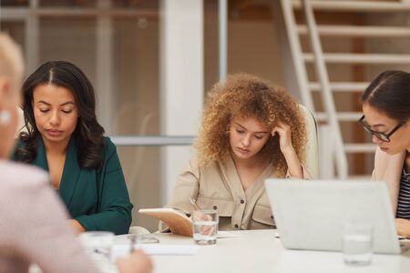 Horizontal eye level shot of pensive young businesswomen doing their job together sitting at office tableの写真素材
