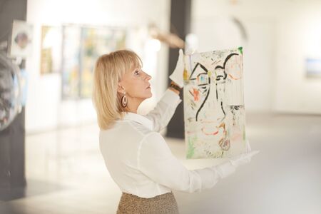Portrait of female art expert holding painting while appraising works in modern gallery or museum, copy spaceの写真素材
