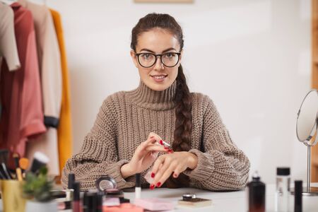 Portrait of smiling young woman testing makeup products and looking at camera while filming video review or tutorial for beauty and lifestyle channel, copy spaceの写真素材