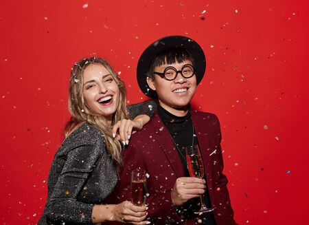 Waist up portrait of trendy young couple holding champagne glasses and smiling happily while...