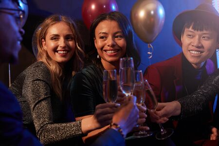 Waist up portrait of elegant young women clinking champagne glasses during party in nightclub