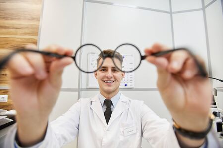 POV shot of smiling young optometrist putting on glasses on unrecognizable patient during vision test in modern clinic, copy spaceの写真素材