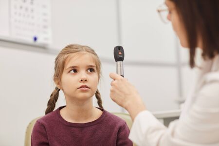 Close up portrait of cute little girl looking at female optometrist during vision test in pediatric ophthalmology clinic, copy spaceの写真素材
