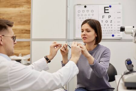 Portrait of male optometrist giving glasses to female patient during vision check in modern clinic,...