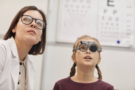 Portrait of cute teenage girl wearing trial frame during childs vision test in modern ophthalmology...