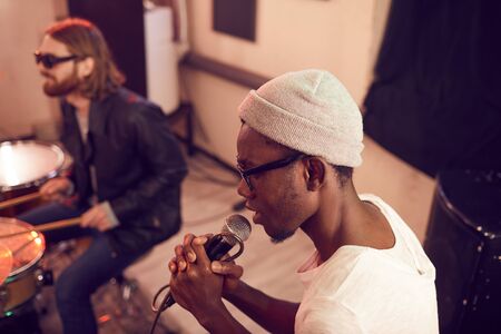 High angle portrait of contemporary African-American man singing to microphone during rehearsal or concert in music studio, copy spaceの写真素材