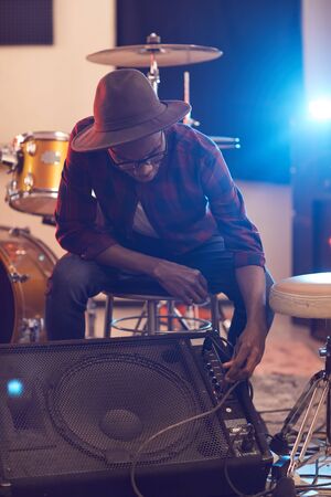 Full length portrait of contemporary African musician setting up guitar amplifier during sound check while preparing for concert or rehearsal with band in backgroundの写真素材