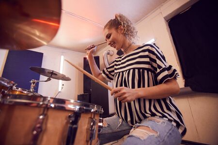 Low angle portrait of smiling young woman playing drums with contemporary music band during rehearsal or concert in studio, copy spaceの写真素材