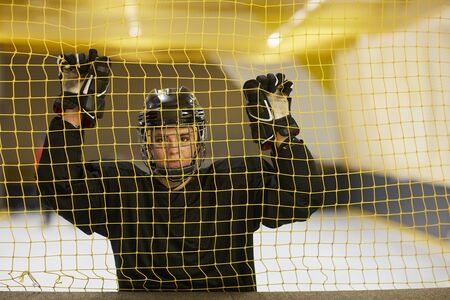 Waist up portrait of female hockey player looking at camera while standing behind gate net on rink,...