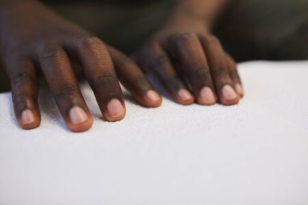 Close up of unrecognizable blind African man reading braille book while studying in school, copy spaceの写真素材