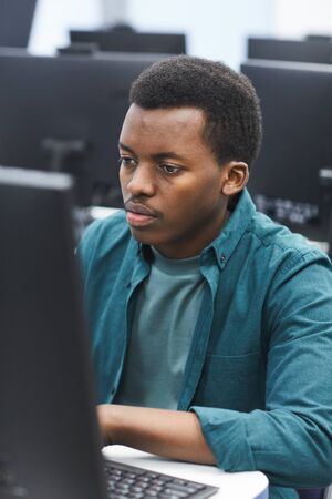 High angle portrait of African-American man using computer in class of college library, copy space