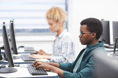 Side view portrait of African-American man using computer in class of college library, copy space