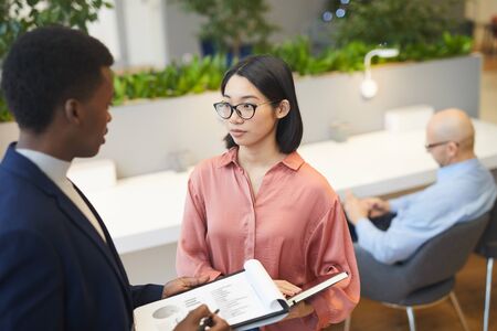 High angle view at young Asian businesswoman talking to partner while discussing project in modern office, copy spaceの写真素材