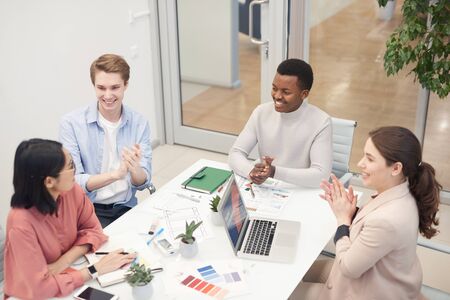 High angle view at multi-ethnic group of business people clapping to Asian colleague while...