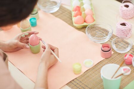 High angle close up of unrecognizable woman painting Easter eggs in pastel colors while sitting at table in kitchen or art studio, copy spaceの写真素材