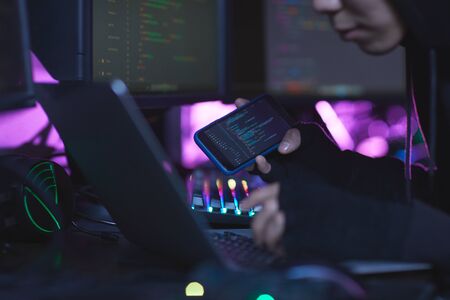 Close up of unrecognizable cyber security hacker wearing hood while working on programming in dark...