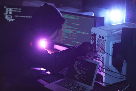 Side view at unrecognizable cyber security hacker wearing hood while working on computer system in dark room, copy spaceの写真素材
