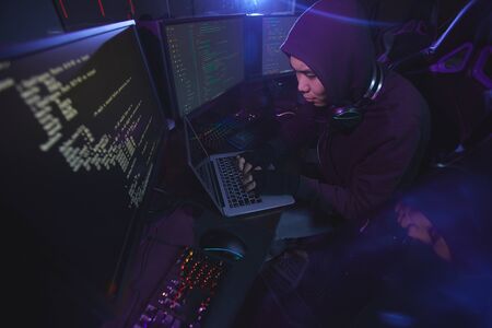 High angle view at Asian cyber security hacker wearing hood while working on programming in dark...