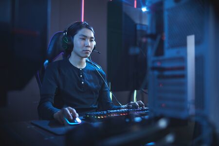 Portrait of young Asian man using computer in dark cyber interior, copy spaceの写真素材