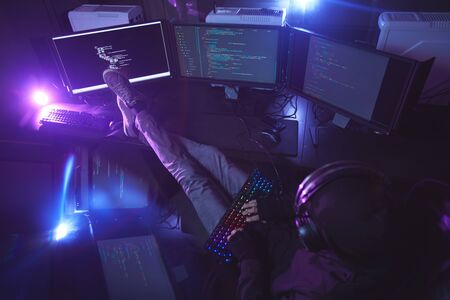 Top view at young man surrounded by multiple screens programming or hacking security in dark room, copy spaceの写真素材