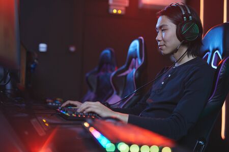 Side view portrait of smiling Asian man playing video games in pro-gaming studio, copy spaceの写真素材