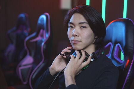 Portrait of young Asian man looking at camera while playing video games in pro-gaming studio, copy spaceの写真素材