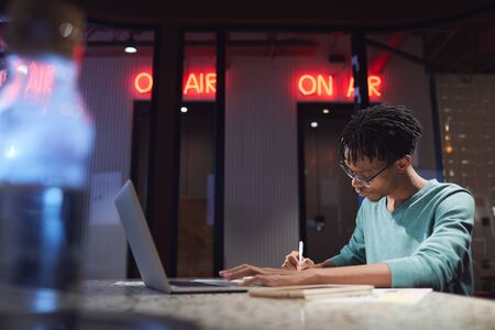 Side view portrait of young African-American man working late at home or in dark office, copy space