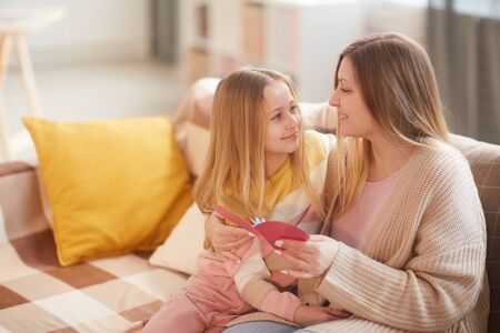 Portrait of blonde little girl embracing mom while celebrating Mothers day together sitting on cozy...