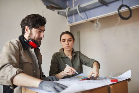 Portrait of young woman looking at floor plans with building contractor while while discussing home renovations, copy spaceの写真素材
