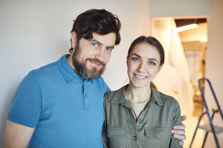 Portrait of happy married couple embracing and looking at camera while renovating house together, copy spaceの写真素材