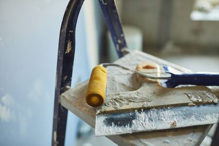Background image of used spatula and paint roller lying on top of ladder on construction site or in house building, copy spaceの写真素材
