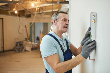 Side view portrait of senior construction worker leveling wall while renovating house, copy spaceの写真素材