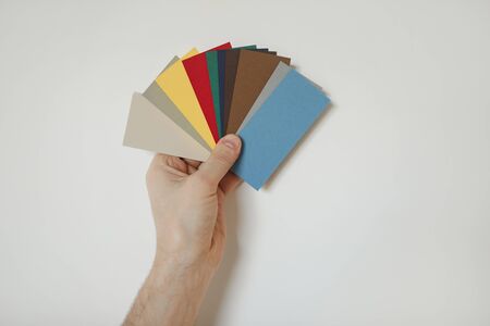 Close up of make hand holding color samples to white wall while choosing design for house redecorations, copy spaceの写真素材