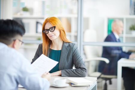 Portrait of adult red haired businesswoman interviewing young man for job vacancy in office, copy spaceの写真素材
