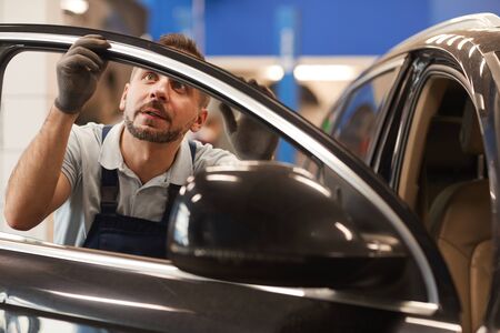 Portrait of mature mechanic checking insulation on windows of luxury car in auto repair workshop, copy spaceの写真素材