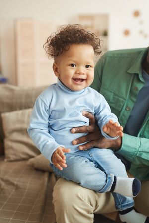 Full length portrait of cute mixed-race baby laughing happily looking at camera while sitting on...